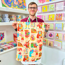 Load image into Gallery viewer, Arthouse Unlimited artist holding the Hugging Animals illustrated tea towel, showcasing organic cotton kitchen gift design made in the UK.