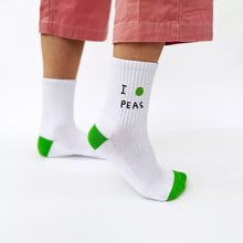 Load image into Gallery viewer, White socks with green accents and text 'I PEAS' worn by a person on a white background