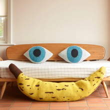 Load image into Gallery viewer, Two blue eye cushions on a sofa with a large banana shaped cushion underneath