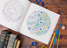 Load image into Gallery viewer, Adult colouring book with a completed floral design on a wooden surface with coloring pencils and books.