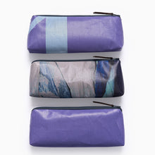 Load image into Gallery viewer, Stacked recycled exhibition banner pencil cases showing different purple and blue graphic design variations.