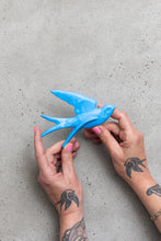 Load image into Gallery viewer, Blue swallow bird wall decoration held by Anna Campbell Jones's hands with tattoos on arm of swallows on a grey concrete background