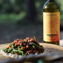 Load image into Gallery viewer, Bottle of Olive Odyssey Marda Palestine extra virgin olive oil with a dish of salad on a wooden surface outdoors.