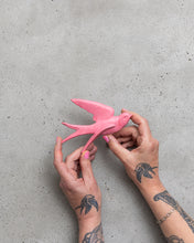 Load image into Gallery viewer, Anna Campbell Jones holding a pink swallow bird decoration for the wall against a grey background