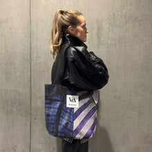 Load image into Gallery viewer, Female model wearing the recycled banner portrait tote bag from the Upcycled by V&A Dundee collection