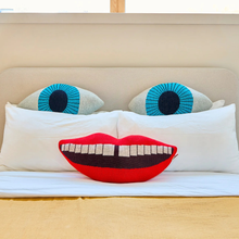Load image into Gallery viewer, two knitted eye cushions on a bed with a large smiley face with red lips cushion on a bed