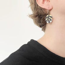 Load image into Gallery viewer, Person wearing a black earring with a gold and black leaf design on a plain background