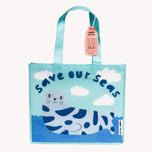 Load image into Gallery viewer, A blue tote bag featuring an illustration of a seal and the text 'Save our seas'. The bag has two blue handles and a tag with the brand name 'Selkie' is visible.