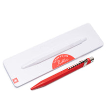 Load image into Gallery viewer, A red Caran D'ache roller pen displayed next to its white metal presentation case with the Caran D'ache logo on the front.