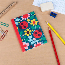 Load image into Gallery viewer, A6 ladybird notebook displayed on a desk with pencils and stationery.
