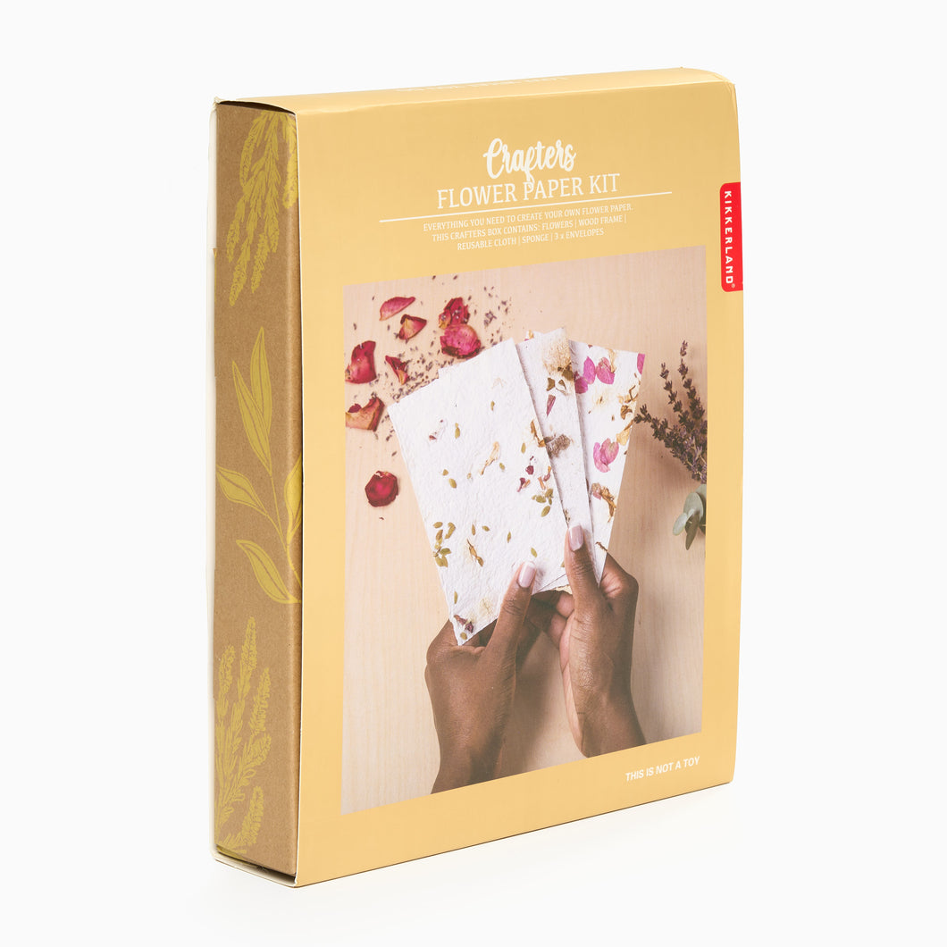 A boxed Paper Making Kit by Crafters, featuring a person holding floral paper within a wooden frame, with flowers and a sponge also visible in the box.