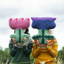 Load image into Gallery viewer, Two people wearing knitted sweaters with holding a thistle shaped cushion and a flower shaped cushion in an outdoor natural setting.
