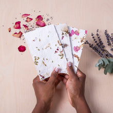 Load image into Gallery viewer, Hands holding crafted flower paper with scattered flower petals and a sponge with lavender in the background
