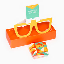 Load image into Gallery viewer, Colorful cardboard glasses with a Sherlock Holmes card and geometric-patterned cards on an orange box.
