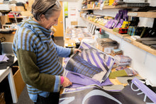 Load image into Gallery viewer, Studio production of upcycled exhibition banner tote bags made from recycled PVC banners in Scotland. Designer looking at swatches
