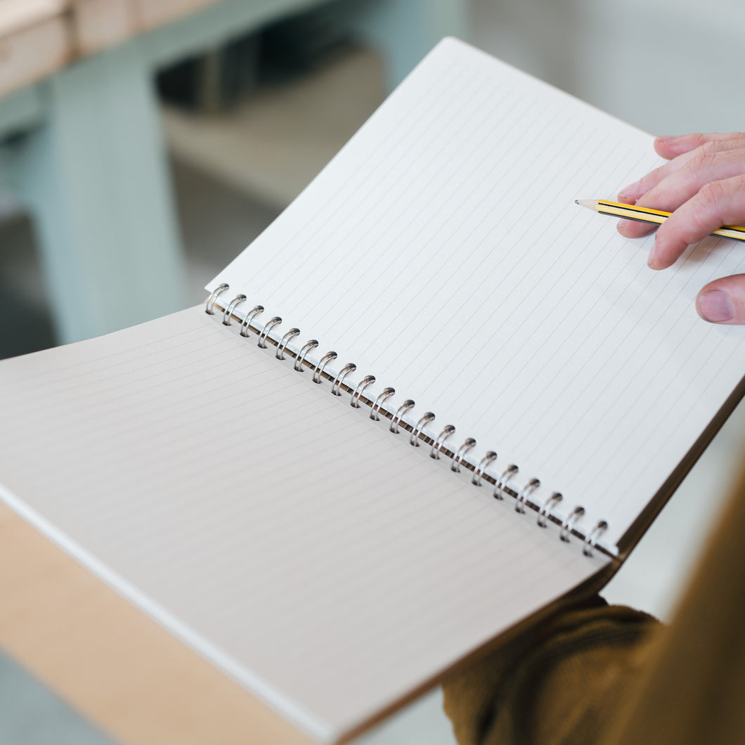 Person holding a spiral-bound notebook with a pen, blurred background