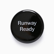 Glossy black Runway Ready pin badge with white lettering.
