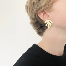 Load image into Gallery viewer, Person wearing silver leaf-shaped earrings on a plain background
