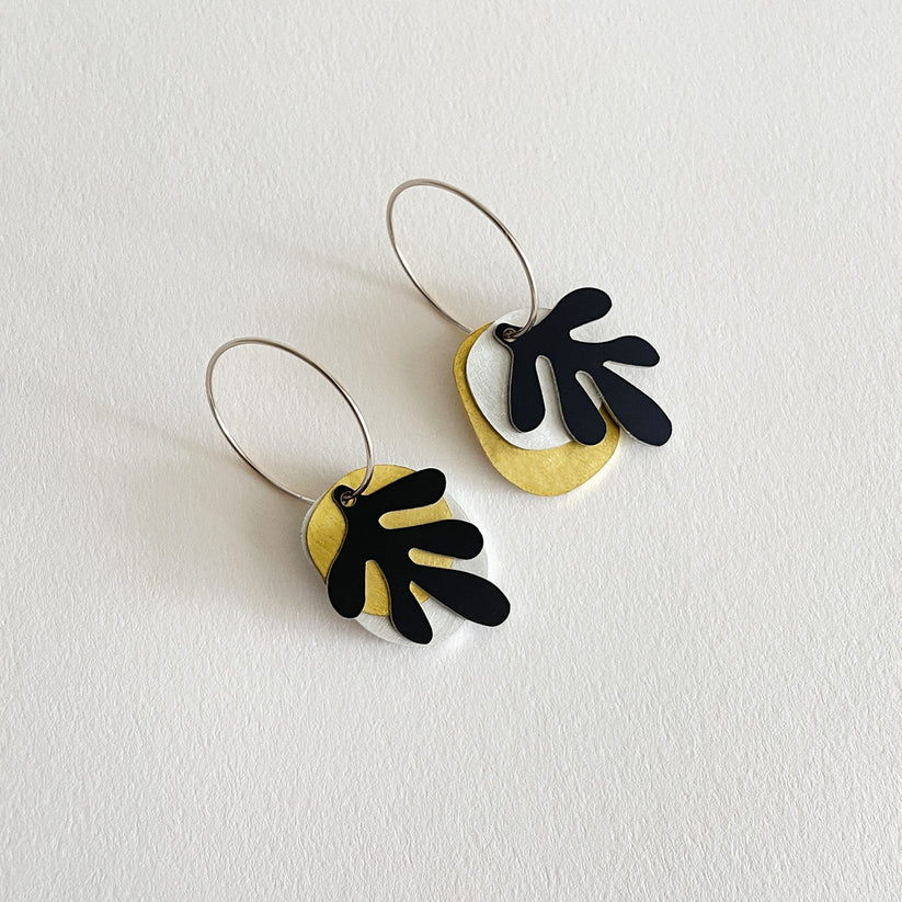 A pair of Tideline earrings with matte anodised aluminium, brushed aluminium, brass, and sterling silver components, presented on a white background.