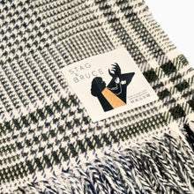 Load image into Gallery viewer, A checkered wool blanket with fringes, predominantly in shades of blue and white, with a brand label showing.

