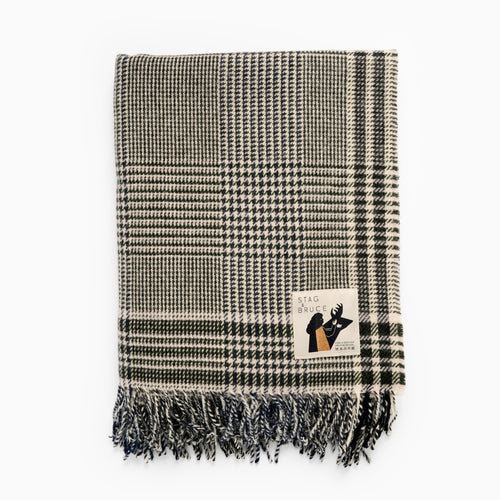 A checkered wool blanket with fringes, predominantly in shades of blue and white, with a brand label showing.