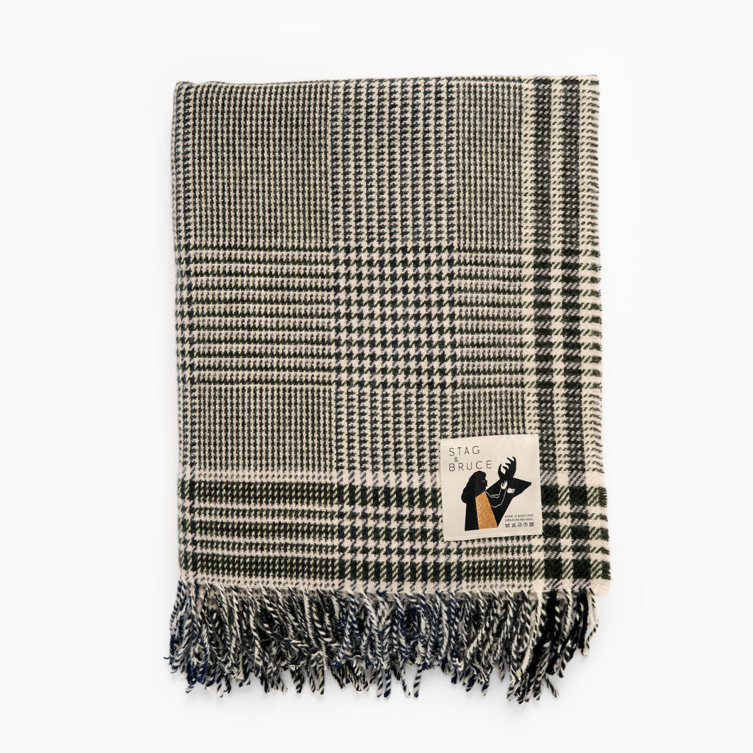 A checkered wool blanket with fringes, predominantly in shades of blue and white, with a brand label showing.