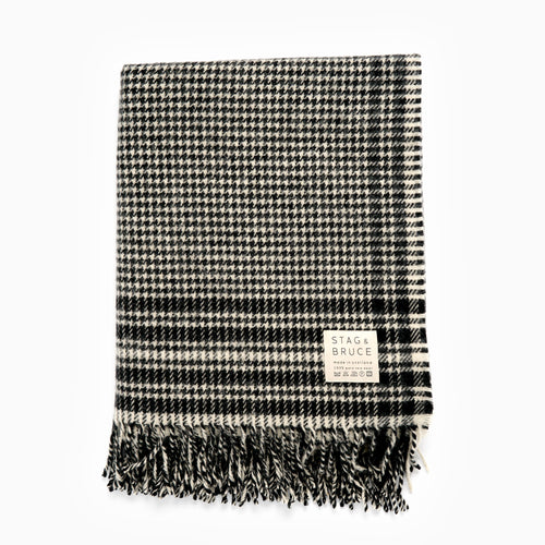 A black and white checkered wool blanket with fringes, displaying the Stag and Bruce brand tag.