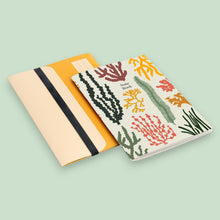 Load image into Gallery viewer, A5 notebook by Studio Wald front cover with coloured illustrations of seaweed sitting on a A5 folder. 
