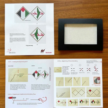 Load image into Gallery viewer, Embroidery kit with patterned paper, black frame, and step-by-step instructions on a wooden surface.
