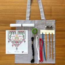 Load image into Gallery viewer, Grey tote bag with embroidery supplies including thread and patterns on a wooden surface
