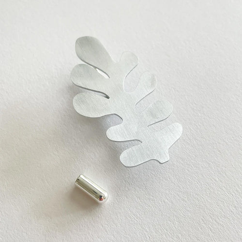 aluminium silver leaf shaped brooch pin on light grey background background
