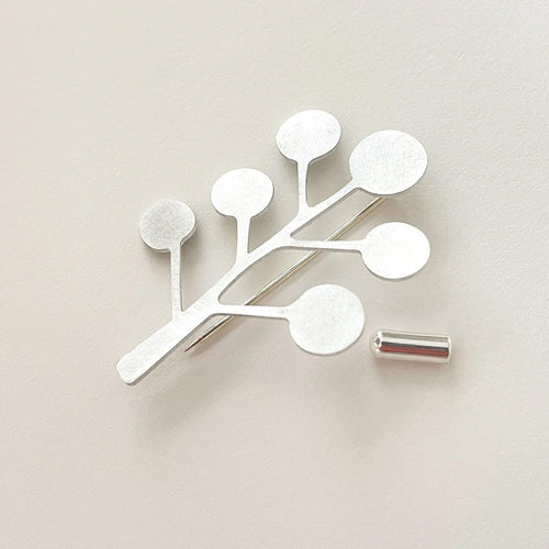 Decorative silver brooch pin with branch-like design on a beige background