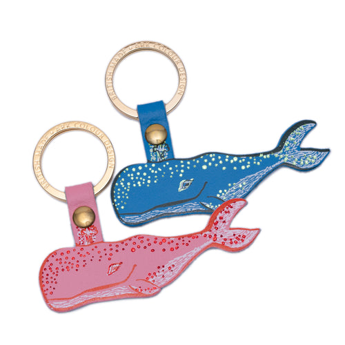 Two leather keyrings designed in the shape of whales, one in blue and one in pink, with metallic foil details.
